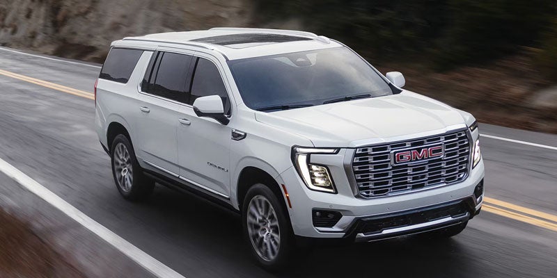 2026 GMC Yukon driving on a scenic highway showcasing its bold exterior design in Clinton, NC